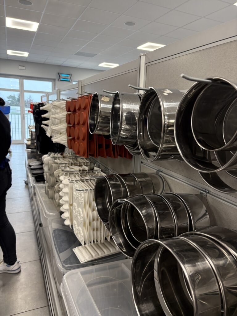 Metalowe obręcze i formy cukiernicze ułożone na półkach w pracowni.