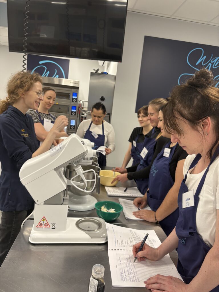 Uczestniczki szkolenia pracują przy mikserze planetarnym i notują przepis.