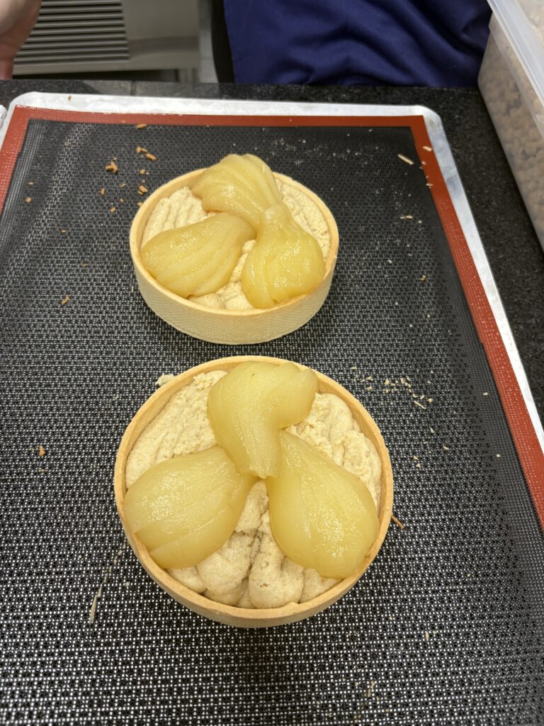 Gotowe tartaletki z kremem i połówkami gruszek ułożone na macie silikonowej.