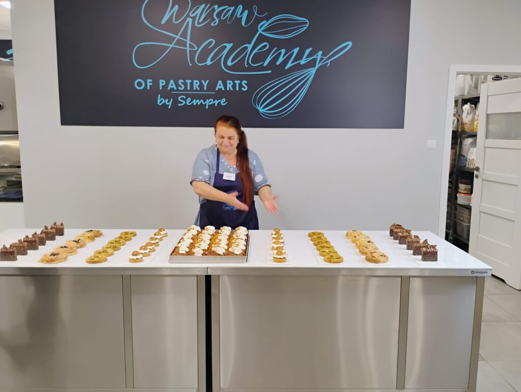 Kobieta stoi przy stole z rzędami gotowych tartaletek w pracowni cukierniczej.